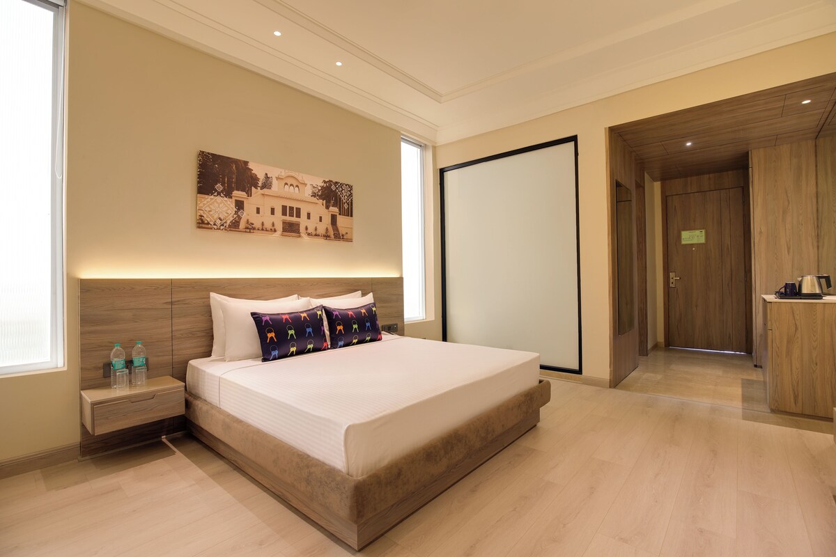 Habitació d'hotel moderna amb un llit gran, una tauleta de nit, una obra d'art penjada a la paret i un armari de fusta.
