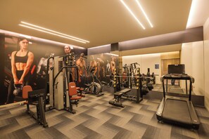 Un gimnasio con diversos equipos de ejercicio, un muro con espejos y una alfombra estampada.