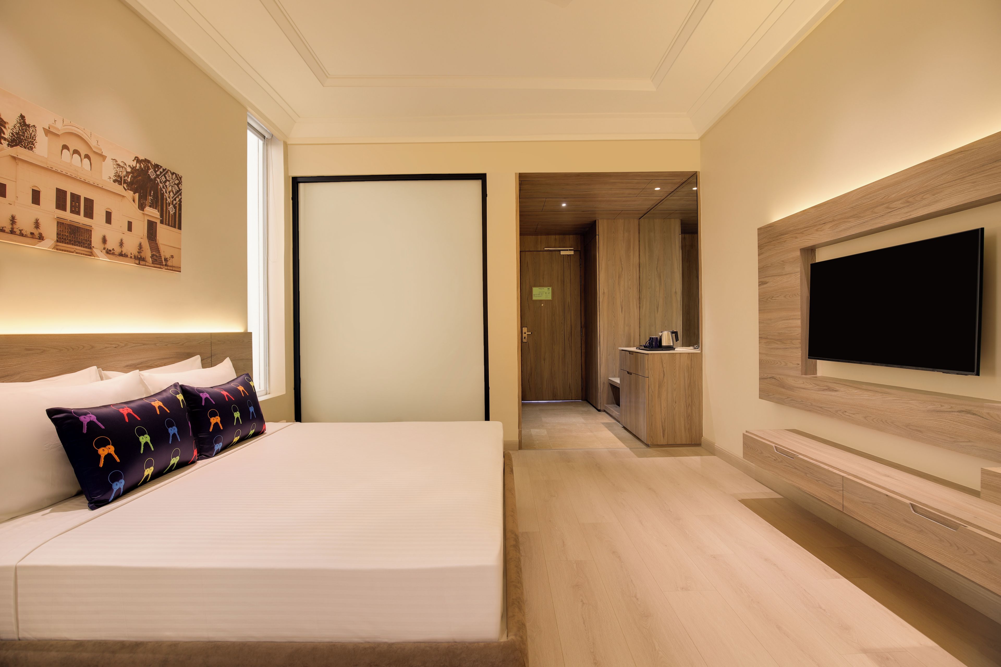 A hotel room with a bed, a TV mounted on the wall, and a view into the kitchen area.
