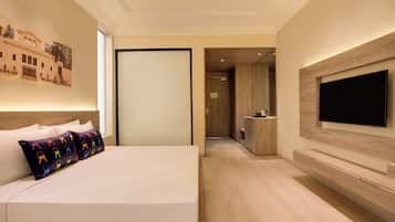 A hotel room with a bed, a TV mounted on the wall, and a view into the kitchen area.