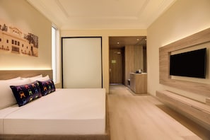 A hotel room with a bed, a TV mounted on the wall, and a view into the kitchen area.