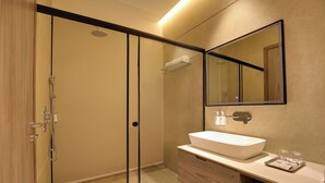 Et moderne badeværelse med en glasvæg omkring brusebadet, et trækommode og et stort spejl.