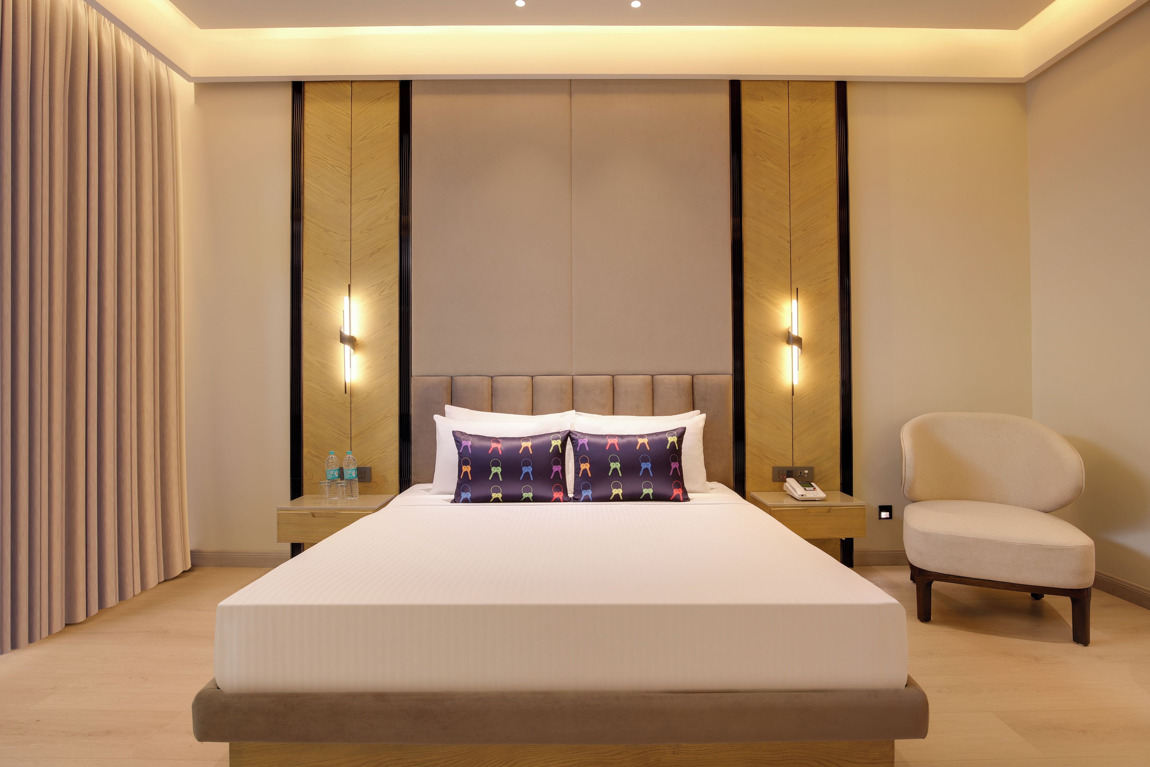 Quarto de hotel com uma cama grande, mesas de cabeceira, uma cadeira e um criado-mudo com telefone.