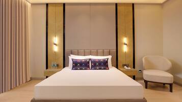 Quarto de hotel com uma cama grande, mesas de cabeceira, uma cadeira e um criado-mudo com telefone.