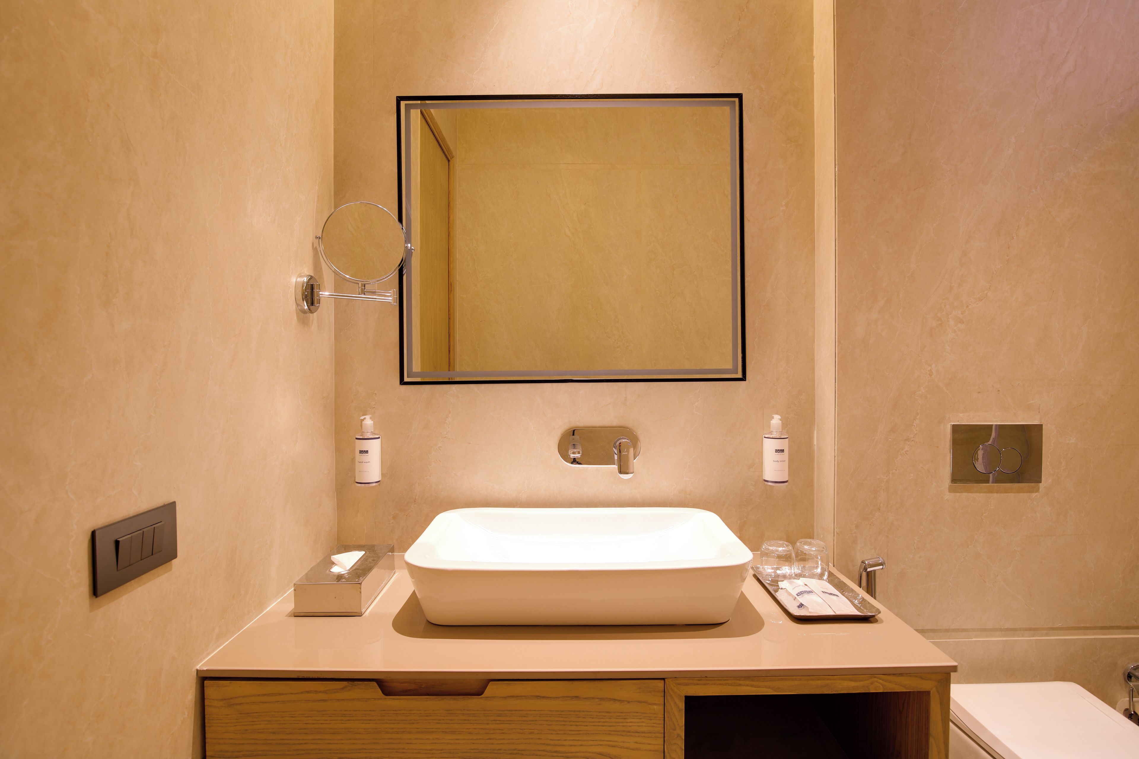 A bathroom with a wooden vanity, a white sink, a mirror, and two bottles of hand soap.