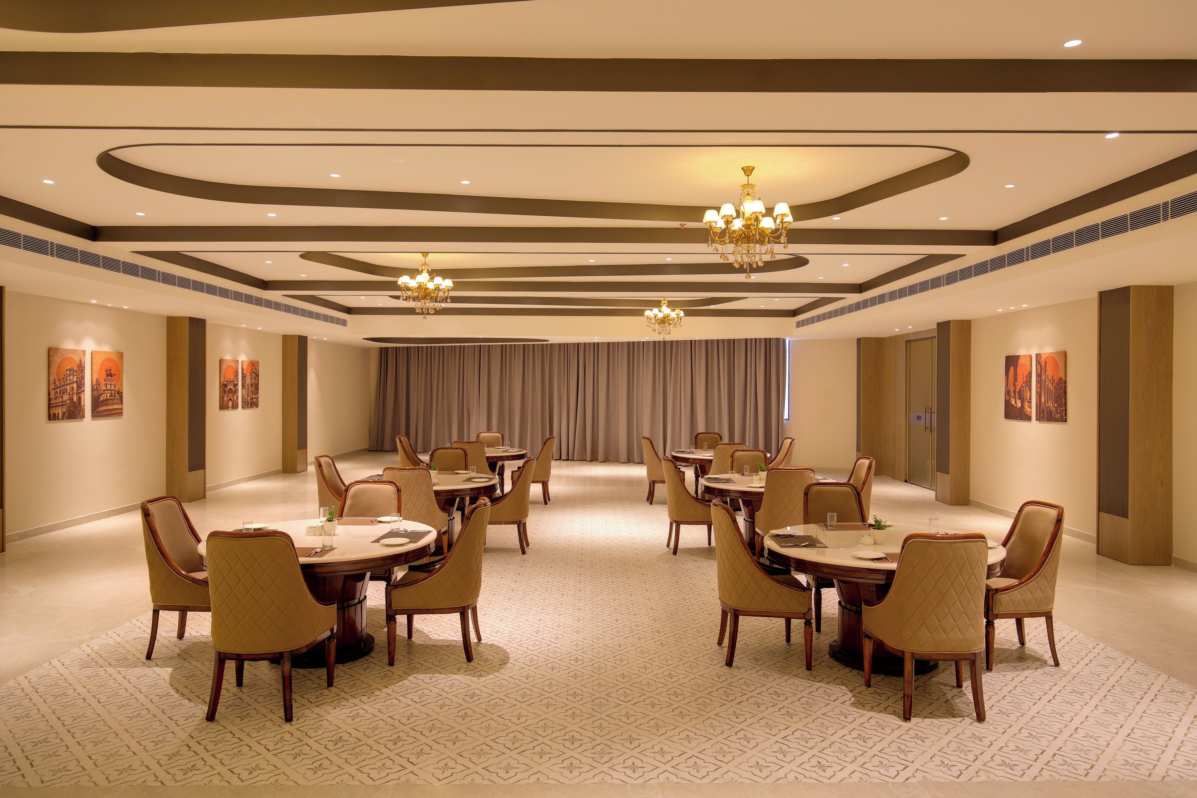 A spacious conference room with round tables and chairs, chandeliers, and artwork on the walls.