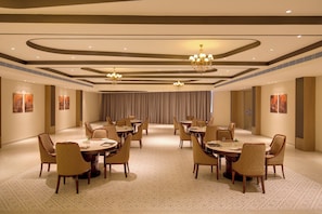A spacious conference room with round tables and chairs, chandeliers, and artwork on the walls.