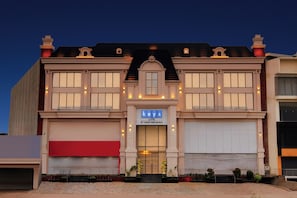 A hotel with a classic architectural design, featuring a central entrance with a sign, large windows, and a red awning on the left.