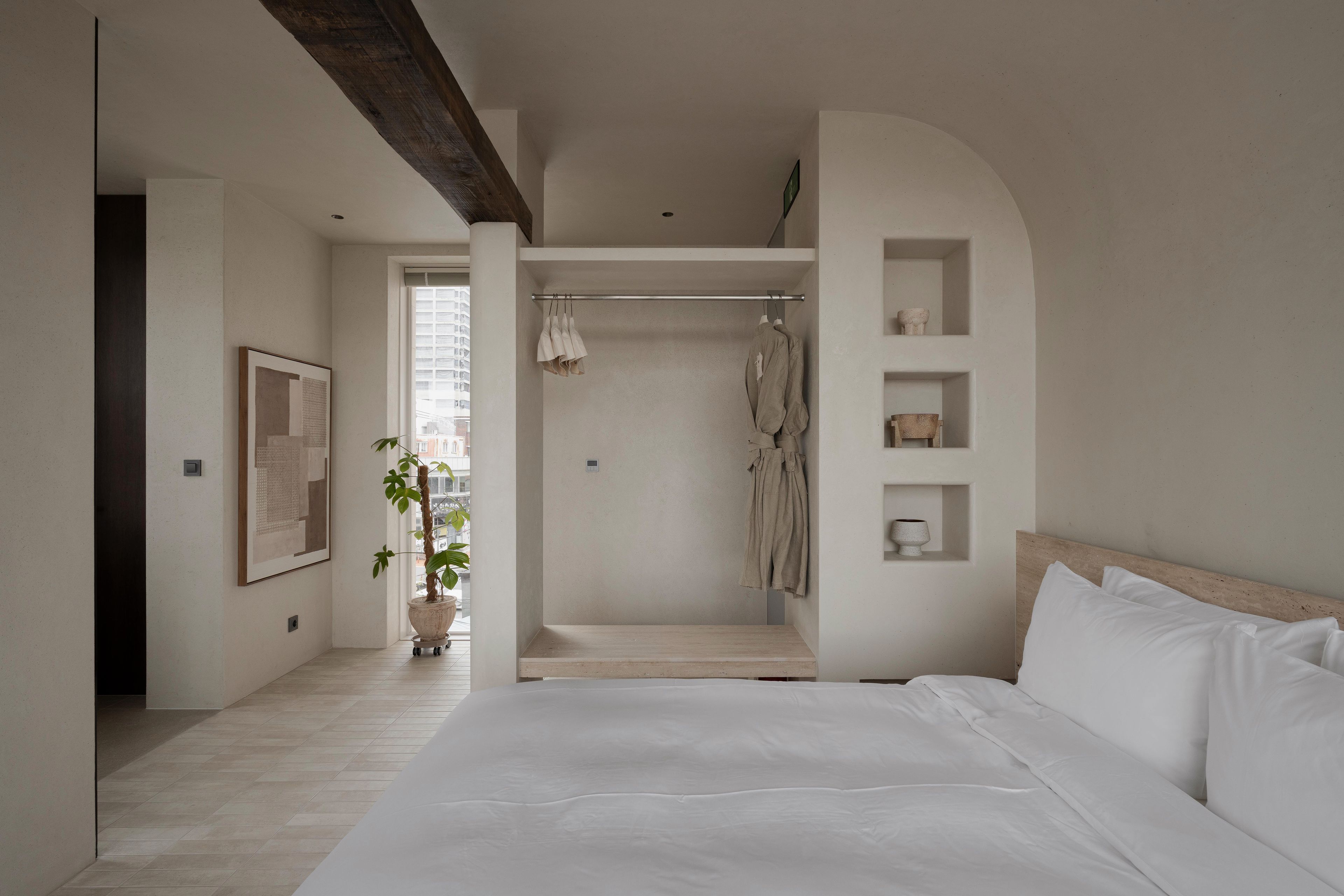 A minimalist bedroom with a large bed, a walk-in closet, and a potted plant.