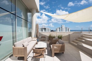 Un área de estar al aire libre con sofá, sillas y una mesa, con vistas a la ciudad y al mar.