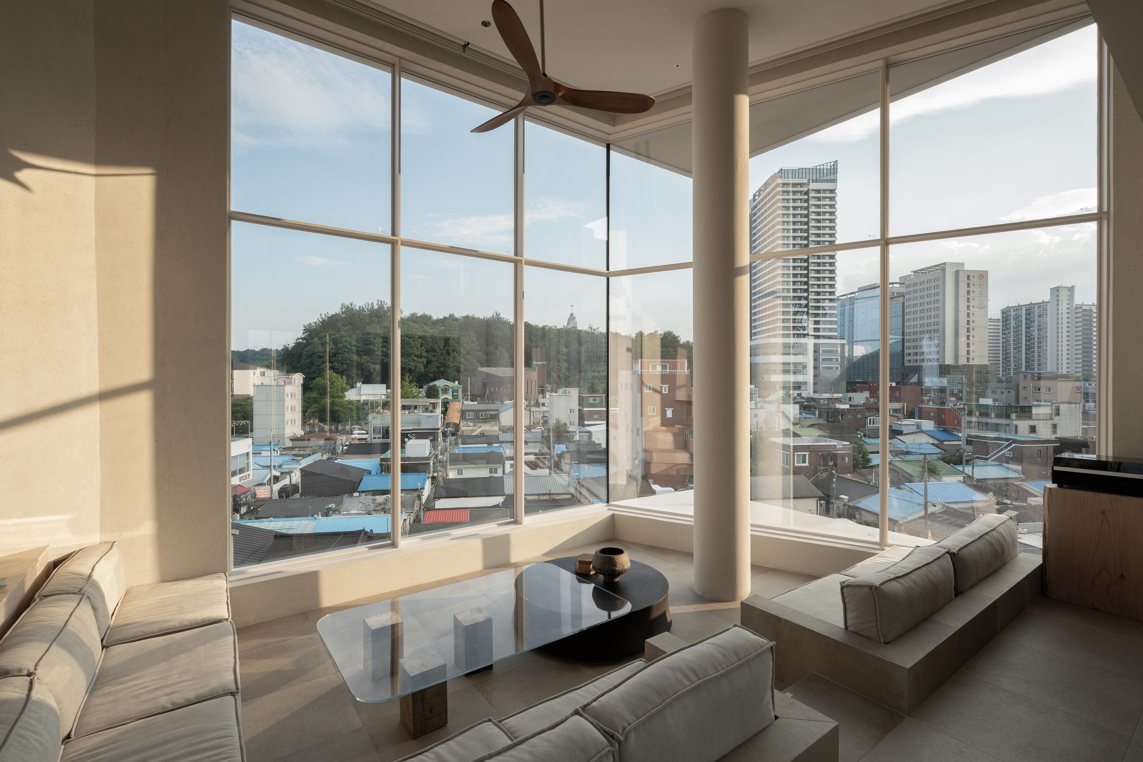 A modern living room with a large window, a ceiling fan, and a sofa.