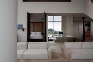 A modern hotel room with a bed, a seating area with sofas, a large window with a city view, and a wooden panel wall. - Stay Oree (Sokcho)