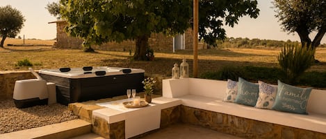 An outdoor seating area with a stone bench, a hot tub, and a pergola.