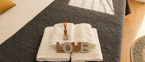 A neatly made bed with a dark patterned bedspread, two folded white towels, and a decorative item spelling 'LOVE' on the bed.