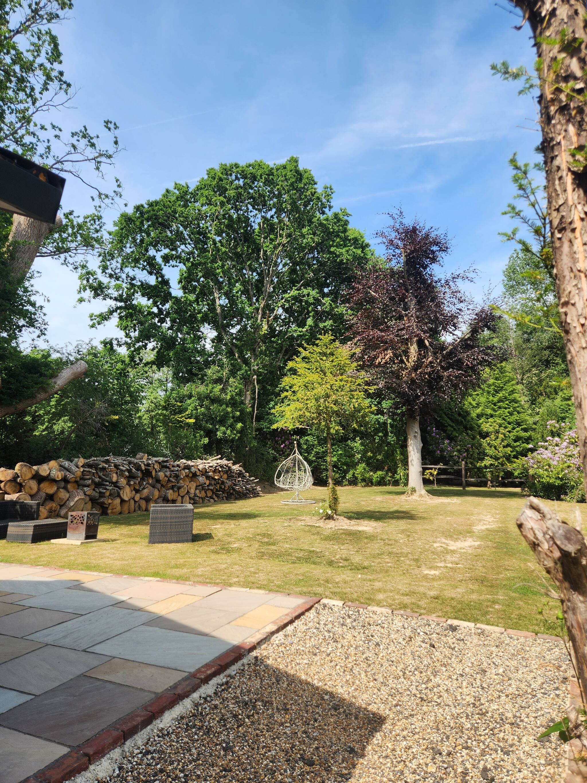 An outdoor area with a stone wall, a pile of logs, and a seating area with wicker furniture.