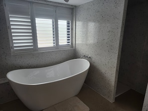 A bathroom with a freestanding bathtub, a window with blinds, and speckled walls. - The PigSty at the Secret Garden (Biddenden)