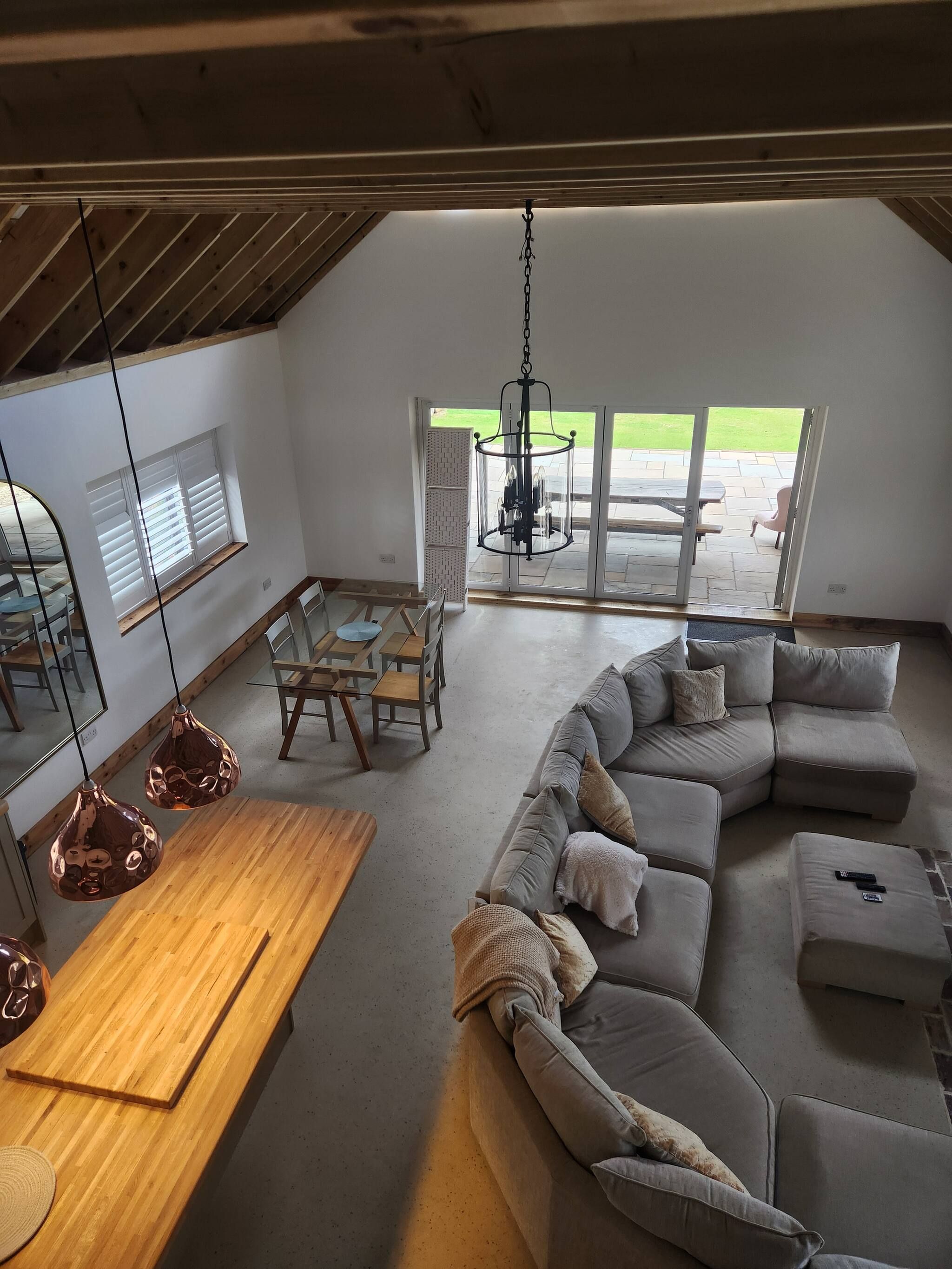 A spacious living area with a large sectional sofa, a wooden dining table, and a hanging light fixture.