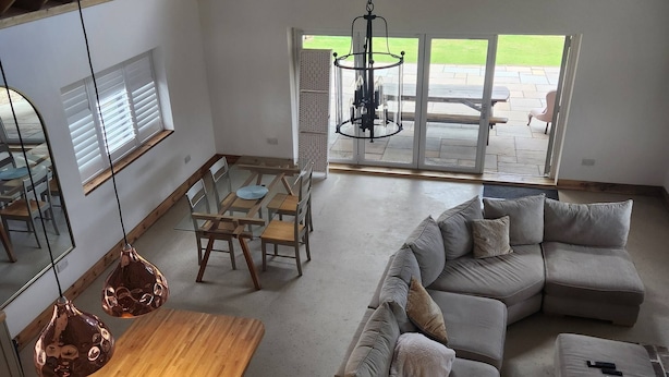 Un amplio espacio de sala con un sofá modular grande, una mesa de comedor de madera y una lámpara colgante.