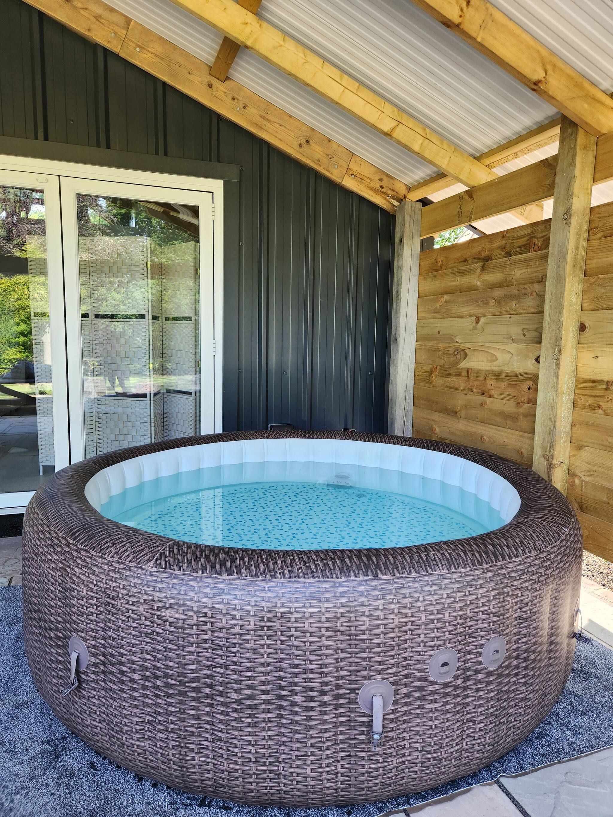 A hot tub with a wicker exterior, a glass door, and a wooden ceiling.
