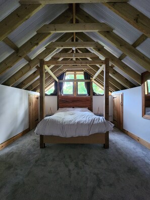 A bedroom with a wooden ceiling, a large bed, and a window. - The PigSty at the Secret Garden (Biddenden)