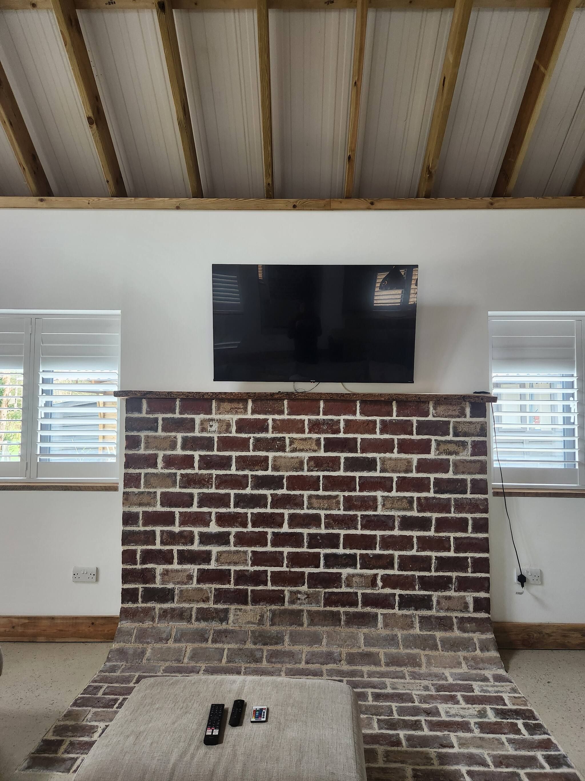 A room with a brick fireplace, a mounted flat-screen TV, and two windows with blinds.