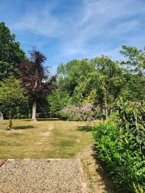 Un jardín bien cuidado con diversas especies de árboles y arbustos, un sendero de grava y una zona verde.