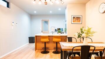 A modern kitchen with a central island, a dining area with a wooden table and chairs, and a small window with frosted glass.