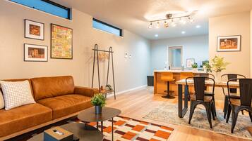 A modern living room with a sofa, coffee table, and a dining area with chairs and a table.