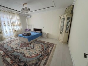 A bedroom with a bed, a nightstand, a cabinet, a chandelier, and a patterned rug. - 2-bedroom apartment in adorable Bukhara with AC comfort (Bukhara)