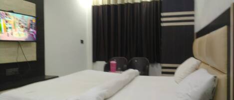 A hotel room with two beds, a television, a window with curtains, and a small table with a pink object.
