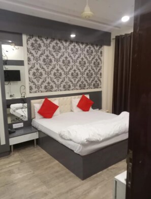 A hotel room with a bed, a bedside table, a mirror, and a patterned wall. - Hotel Ladli Ji Inn (Mathura)