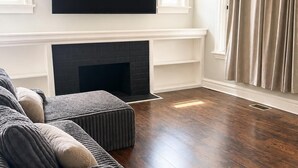 Una sala de estar con una televisión de pantalla plana sobre una chimenea, un sofá modular y un ventilador de techo.