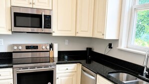 Una cocina moderna con electrodomésticos de acero inoxidable, armarios de color claro y encimera negra.