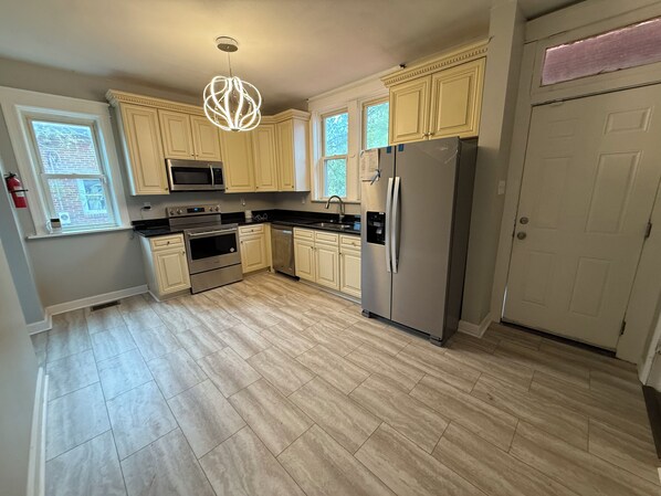 A kitchen with light-colored cabinets, stainless steel appliances, and a modern pendant light.