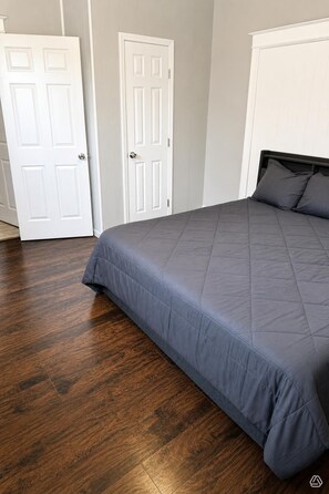 A bedroom with a bed, wooden flooring, and white doors.