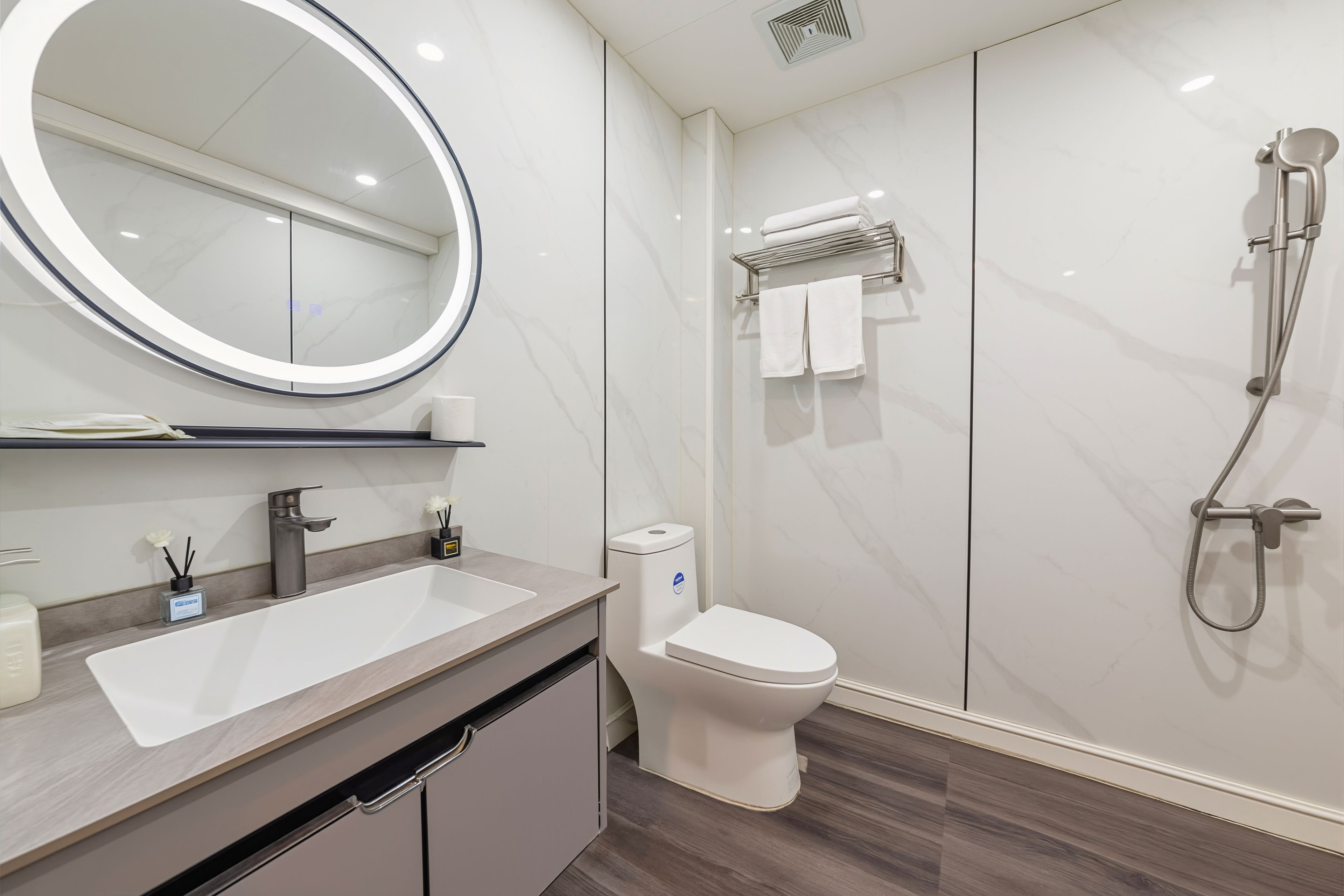 Een moderne badkamer met een ronde spiegel, een wastafel, een toilet en een douche.