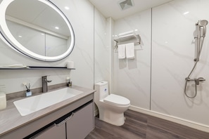 Un baño moderno con un espejo redondo, un lavamanos, un inodoro y una ducha.