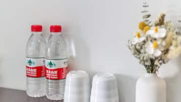 Two clear water bottles with red caps and a white vase with flowers on a table.