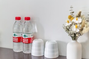 Duas garrafas de água transparentes com tampas vermelhas e um vaso branco com flores sobre uma mesa.