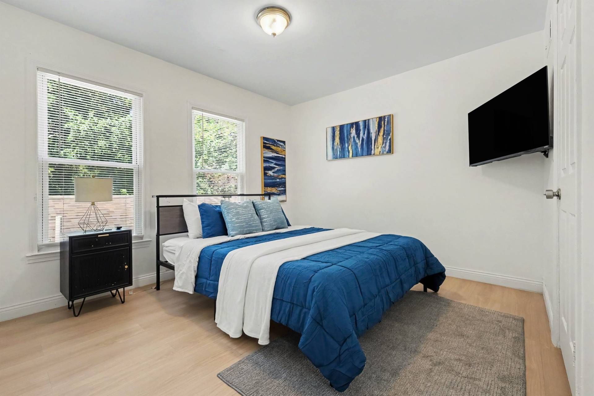 Un dormitorio con cama, mesita de noche, televisor y obras de arte en la pared.