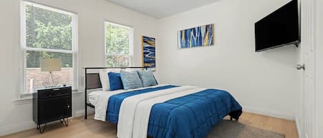 A bedroom with a bed, a nightstand, a TV, and artwork on the wall.