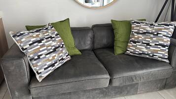Un sofá de cuero gris con dos almohadones estampados y un cojín verde decorativo.