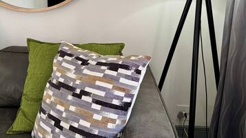 A modern living room with a grey sofa, a patterned throw pillow, a green pillow, a round mirror, and a floor lamp.