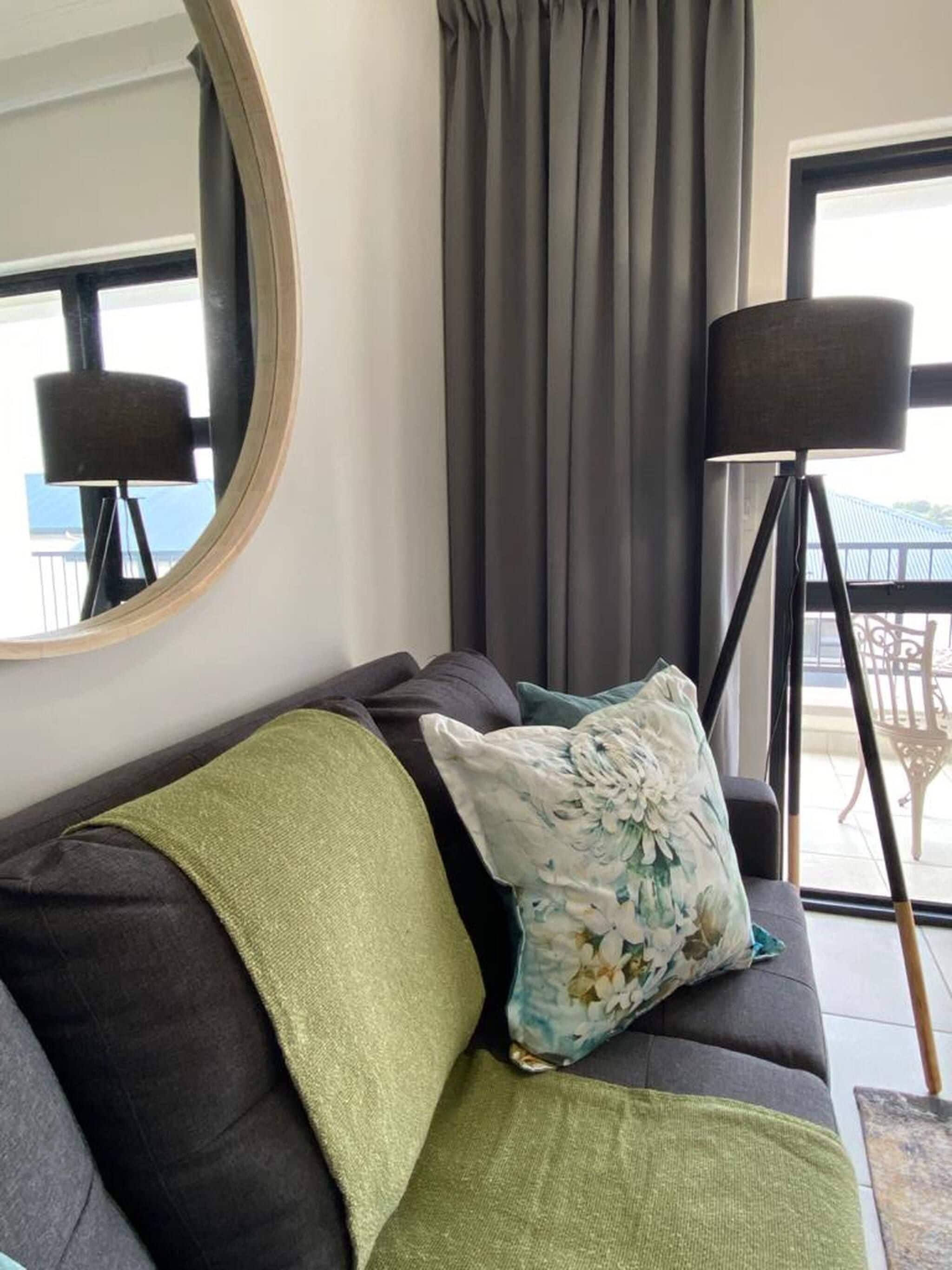 A living room with a sofa, a round mirror, a floor lamp, and a view of the outdoors.