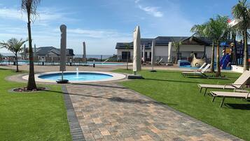 A pool area with lounge chairs, a pathway, and a building with a modern design.