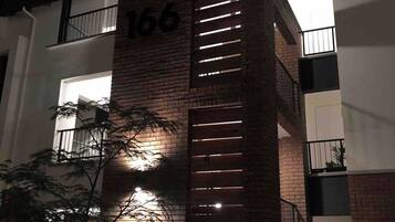 A building with a brick facade, a balcony with metal railings, and the number '166' on the side.