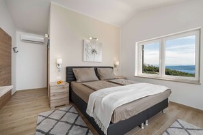 A bedroom with a bed, bedside lamps, a nightstand, a window with a view, and an air conditioning unit. - Villa Mare Visum with heated pool (Ripenda Kosi)