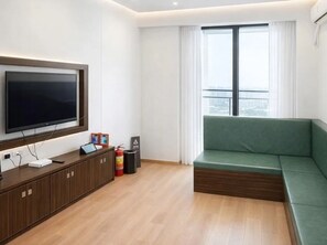 A modern living room with a flat-screen TV, wooden cabinet, green sofa, and a large window with curtains. - Yizhenju Garden Residence Haizhu Wetland (Guang Zhou Shi)