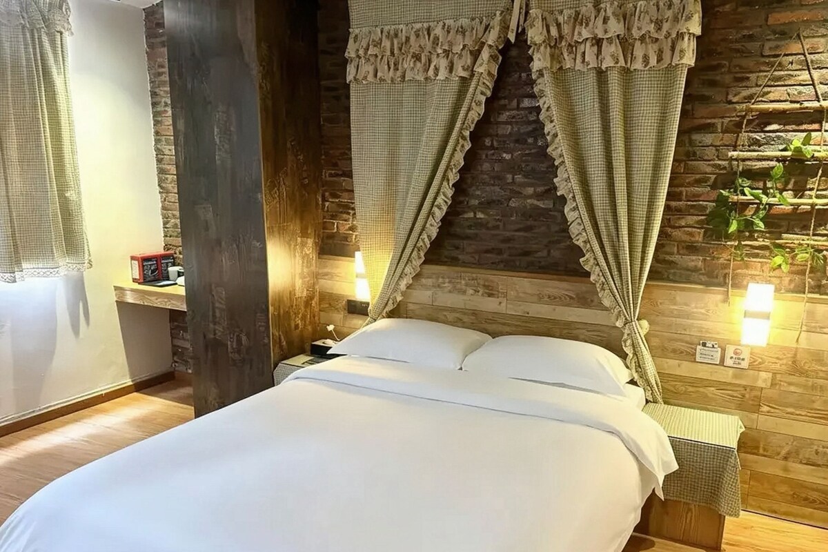 A bed with a white duvet, a wooden headboard, and a stone wall behind.