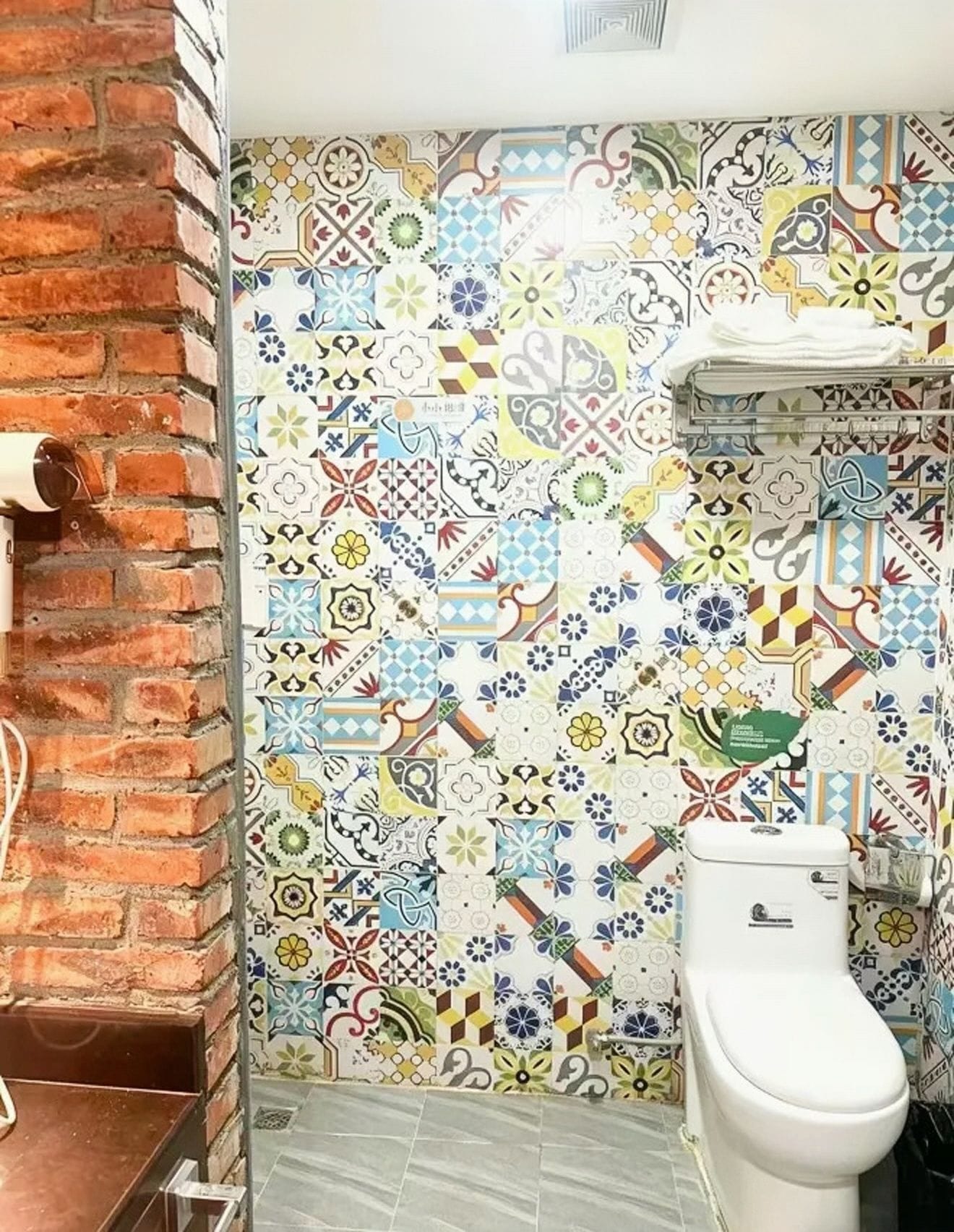 A bathroom with a tiled wall featuring a variety of patterns and a white toilet.